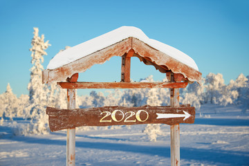 Wall Mural - 2020 written on a wooden direction sign, blue sky and winter snowy tree landscape background happy holiday seasons new year greetings