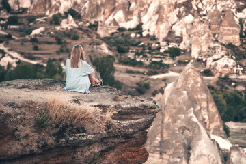 Girl sitting on the top of mountain in Cappadocia, Turkey. Aerial view on the famous stone peaks. Concept of travel and adventure.