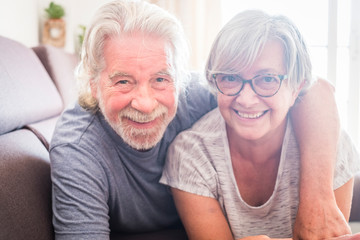 couple of two seniors and mature people lying down on the sofa looking at the camera smiling and lau