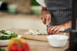 © nenadaksic - Close up of mixed race woman in apron standing in kitchen and chopping mushrooms.
