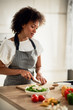 © nenadaksic - Gorgeous mixed race housewife in apron standing in kitchen and chopping mushrooms. On kitchen counter are all sorts of vegetables.