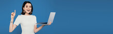 Panoramic Shot Of Excited Smiling Elegant Woman Holding Laptop And Showing Idea Gesture Isolated On Blue