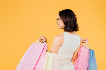 Wall Mural - back view of woman in sunglasses holding shopping bags isolated on yellow