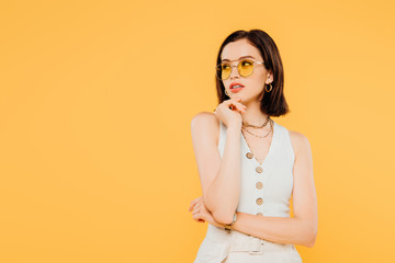 Wall Mural - dreamy fashionable girl in sunglasses looking away isolated on yellow