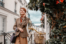 Outdoor Autumn Portrait Of Young Happy Smiling Fashionable Lady Wearing Trendy Brown Leather Beret, Turtleneck, Beige Houndstooth Checkered Blazer, Holding Bag, Posing In Street Of Paris. Copy Space