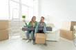 © satura_ - Cheerful joyful young couple charming girl and handsome man holding a box with things and a pot with a plant while moving to a new apartment. Housewarming and mortgage concept.