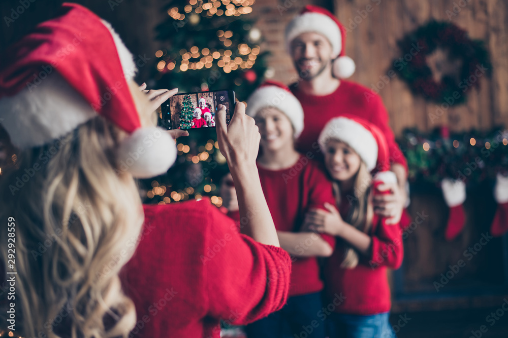 Blurry photo of mom making photo of two children and dad near decorated garland newyear tree indoors family x-mas atmosphere wear santa caps and red sweaters - obrazy, fototapety, plakaty 