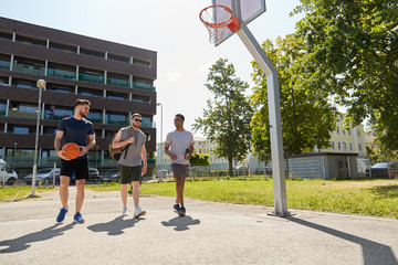 Wall Mural - sport, leisure games and male friendship concept - group of men or friends going to play basketball outdoors