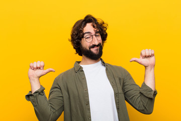 young crazy man feeling proud, arrogant and confident, looking satisfied and successful, pointing to self against yellow wall