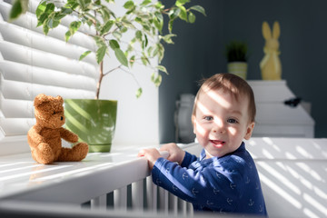 Happy kid near window on white bed in his room