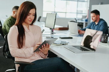 Wall Mural - An attractive young smiling businesswoman using digital tablet with colleagues working at desk in background at office - startup office