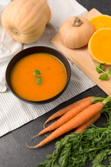 Wall Mural - food, new nordic cuisine, culinary and cooking concept - close up of vegetable pumpkin cream soup in bowl and bunch of carrots on stone table