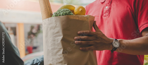Web banner. smart food delivery service man in red uniform handing fresh food to recipient and young customer receiving order from courier at home, food express delivery and online shopping concept
