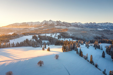 Fototapete - Sunrise in winter mountains. Scenic nature of snowy summits of mountain range illuminated by sun. Aerial view of mountains in sunlight