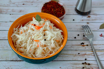 Homemade Sauerkraut with Carrot in a ceramic plate with a fork on a white wooden table. Fermented food. Copy space. Healthy food. Fermented preserved vegetarian food,