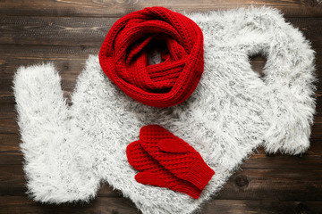 Wall Mural - Knitted sweater with red scarf and pair of gloves on wooden table