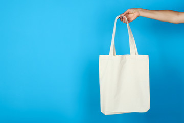 Poster - Female hand holding white cotton eco bag on blue background