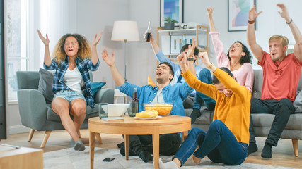 Wall Mural - At Home Diverse Group of Sports Fans Sitting on Couch Watching Important Sports Game Match on TV, They Cheer for Team, Celebrate Victory after Team Scoring Winning Goal. Cozy Room with Snacks Drinks.