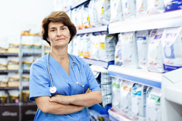 Portrait of confident elderly woman veterinarian standing near shelves with dog food in pet supplies store