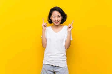 Asian young woman over isolated yellow wall pointing up a great idea