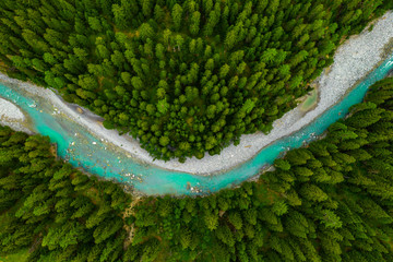 Inn River flowing in the forest in Switzerland. Aerial view from drone on a blue river in the mountains