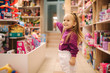© Aleksandr - Adorable little girl shopping for toys. Cute female in toy store. Happy young girl selecting toy