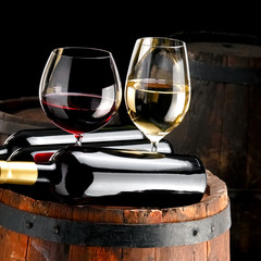 Red and white wine glasses and bottles over a old wine barrel, close up