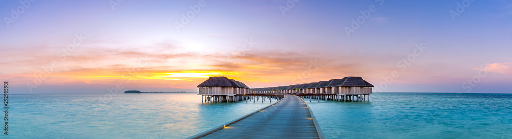 Amazing sunset panorama at Maldives. Luxury resort villas seascape with soft led lights under colorful sky. Beautiful twilight sky and colorful clouds. Beautiful beach background for vacation holiday - obrazy, fototapety, plakaty 