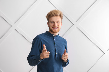 portrait of young man pointing at viewer on grey background