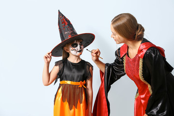 Canvas Print - Mother with little daughter in costumes preparing for Halloween party on light background