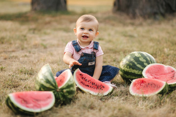 Portrait of beautiful baby girl eating watermelon. Child eating watermelon in the garden. Adorable little girl playing in the garden biting a slice of watermelon