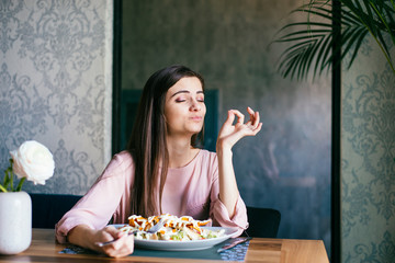 Young lady sitting in a beautiful restaurant, enjoying lunch and gesturing ok sign with her fingers