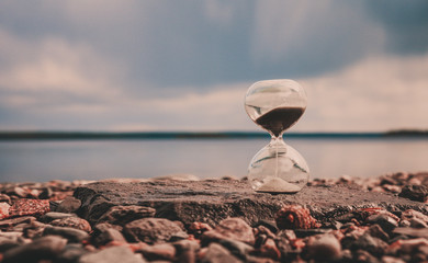 Hourglass on stones near the lake, atmospheric photo of falling sand in a glass clock shape, time concept