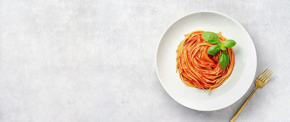 Wall Mural - Top view of plate eith pasta in tomato sauce and basil on white background