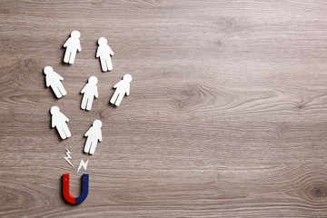magnet attracting paper people on wooden background, flat lay. space for text
