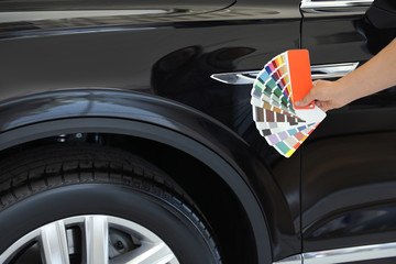 Poster - Young woman holding palette with color samples near black car, closeup