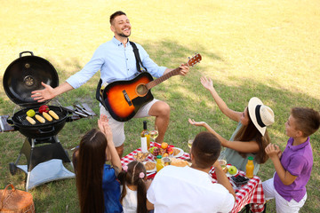 Poster - Man playing guitar for friends at picnic in park