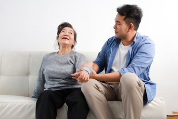 Wall Mural - Asian senior woman mother and young man son in blue shirt massage his mother in living room