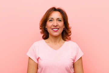 middle age woman smiling positively and confidently, looking satisfied, friendly and happy against pink wall