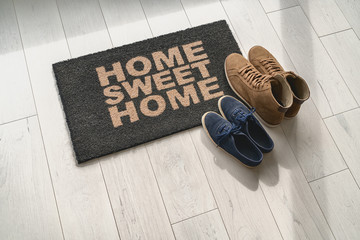 home sweet home doormat at condo door entrance with couples pairs of shoes moving in together. women