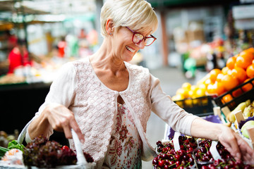 Wall Mural - Picture of mature woman at marketplace buying vegetables