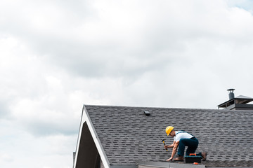 Wall Mural - repairman in helmet holding hammer while repairing roof