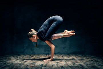 young woman practicing yoga doing forearm stand crane pose asana in dark room
