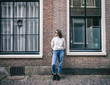 © papa - A stylish young woman in jeans and sunglasses stands on a city street, leaning against a brick wall.