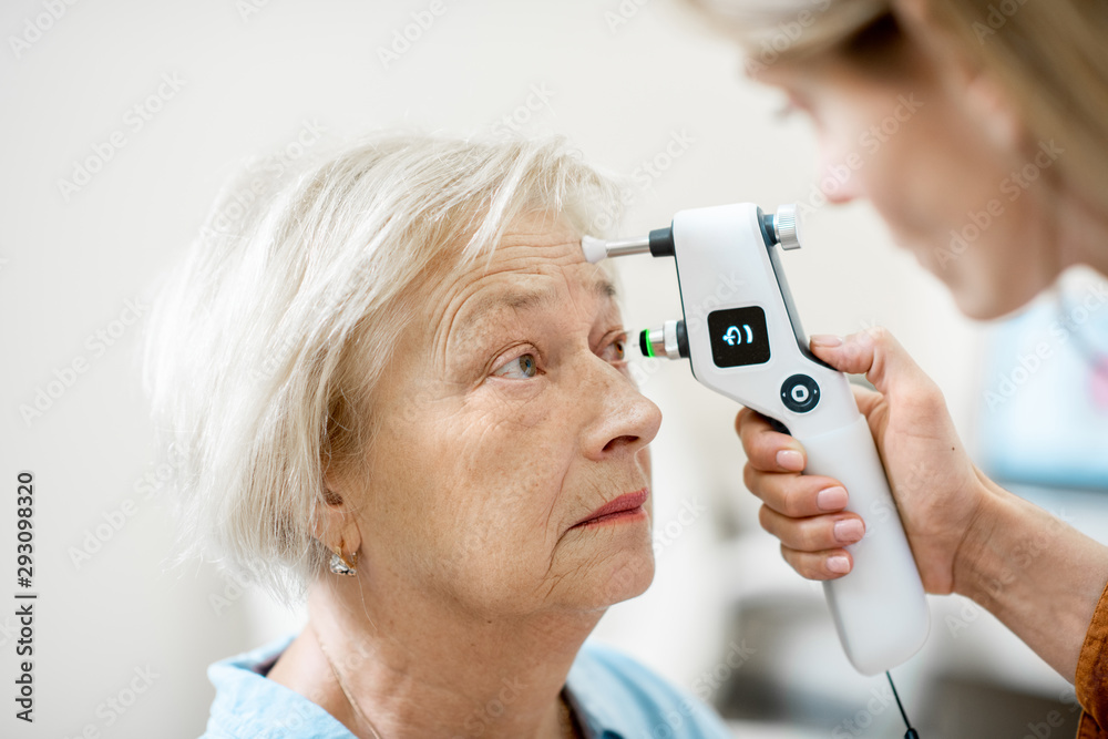Female ophthalmologist measuring the eye pressure with modern tonometer to a senior patient in the medical office, close-up view - obrazy, fototapety, plakaty 