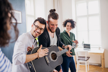 Wall Mural - A group of young friends with guitar indoors at home, house sharing concept.