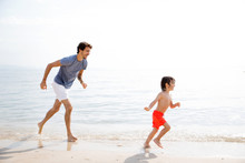Father And Son Happily Running In Water At Beach