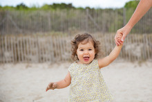 Portrait Of Happy Toddler Holding Mother's Hands While Walking On Sand At Beach