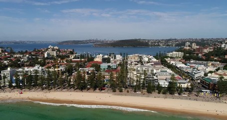 Poster - Sandy Manly beach in Sydney washed by Pacific ocean in aerial panning along waterfront with distant city CBD towers on the horizon.