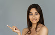 Happy young indian woman beautiful face hold cream on finger look at camera isolated on grey studio background, pretty healthy girl model advertise facial skin care, natural beauty concept, portrait